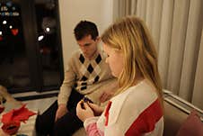 A Woman And A Man Sit In A Dimly Lit Living Room, Both Appearing Deep In Thought. The Woman Holds A Small Object, While The Man Lo Stock Image