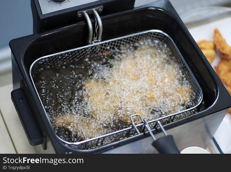 Golden, crispy chicken nuggets frying in hot oil, bubbling and sizzling to perfection. The mouthwatering aroma fills the air as th