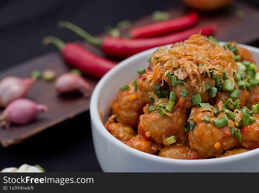 the image shows a close-up of a bowl filled with meatballs covered in a spicy red sauce. the meatballs are garnished with fried onions and chopped green onions. in the background, there are red chilies and shallots on a wooden board, adding to the culinary theme. the overall composition is well-lit and visually appealing, emphasizing the freshness and flavors of the dish. the image shows a close-up of a bowl filled with meatballs covered in a spicy red sauce. the meatballs are garnished with fried onions and chopped green onions. in the background, there are red chilies and shallots on a wooden board, adding to the culinary theme. the overall composition is well-lit and visually appealing, emphasizing the freshness and flavors of the dish.