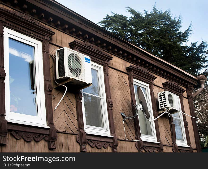 An old wooden house with modern windows and air conditioners in a southern town, the windows reflect the blue sky