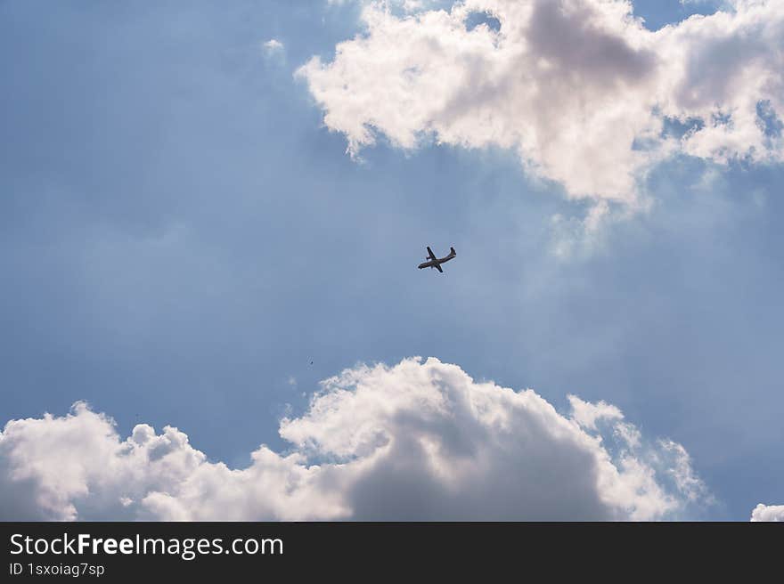 A commercial airplane soars high above, silhouetted against a vast blue sky with scattered clouds. The sunlight filtering through