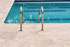 A Stainless Steel Ladder With Curved Handrails Descends Into A Calm Swimming Pool With Clear Blue Water. The Edge Of The Pool Is S Stock Image