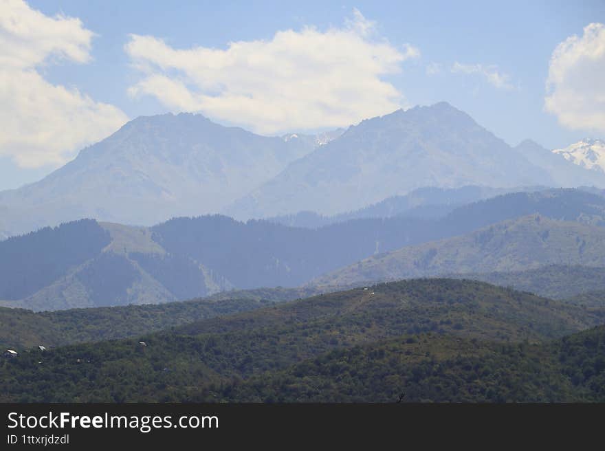 Snow-Capped Peaks and Lush Hillside with Scattered Homes Under a Partly Cloudy Sky: Serene Alpine Living