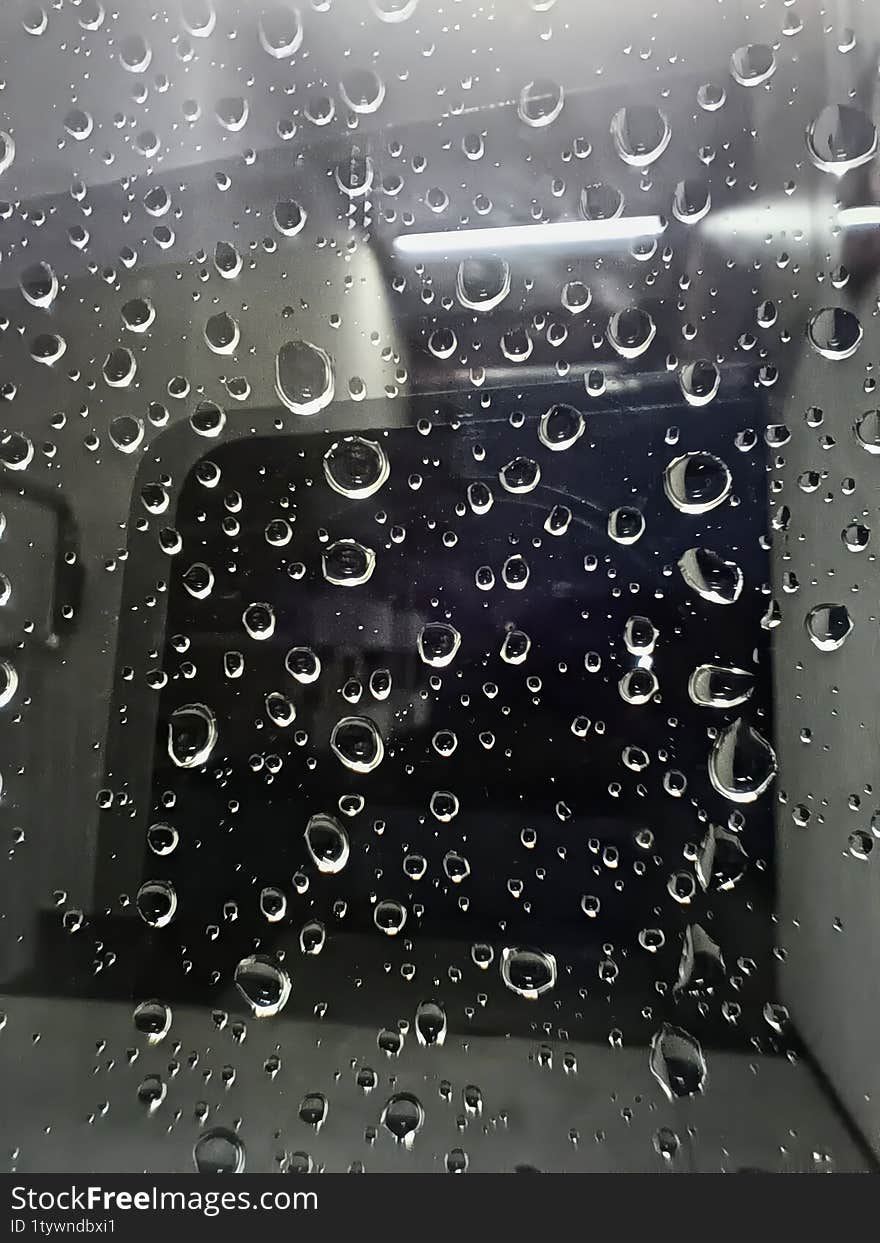 Close-up Droplets Clinging To Glass Surface Of Window Covered In Raindrops, Reflecting Soft Light. Blurred Background Creates Mood