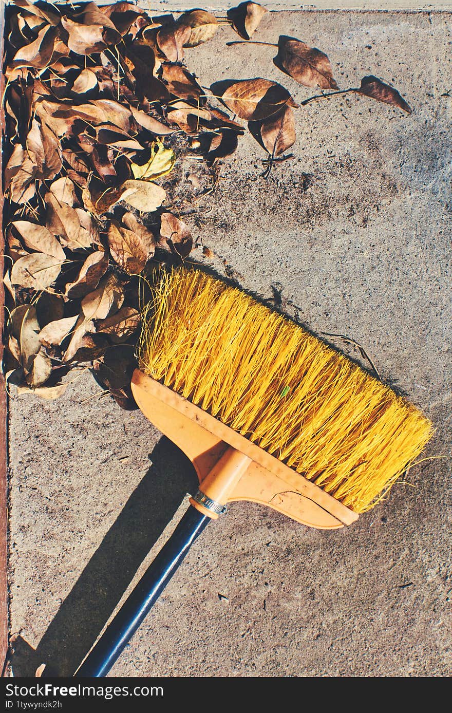 Yellow Broom Resting On A Concrete Surface With Scattered Dry Leaves. Ideal For Autumn, Cleaning, Or Outdoor Themes, Capturing A R