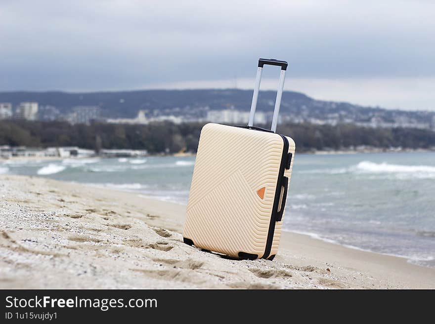 A suitcase stands on a sandy beach by the sea with a cityscape in the background. Perfect for travel, vacation, and adventure concepts.