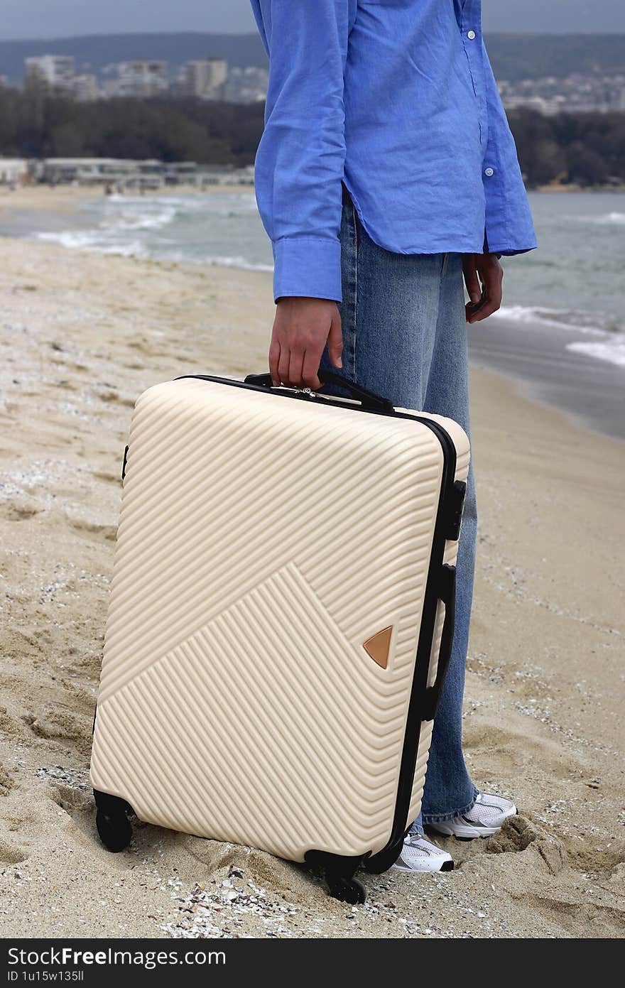 Close-up woman with a suitcase stands by the sea, gazing at the horizon. A symbol of travel, new beginnings, and freedom.