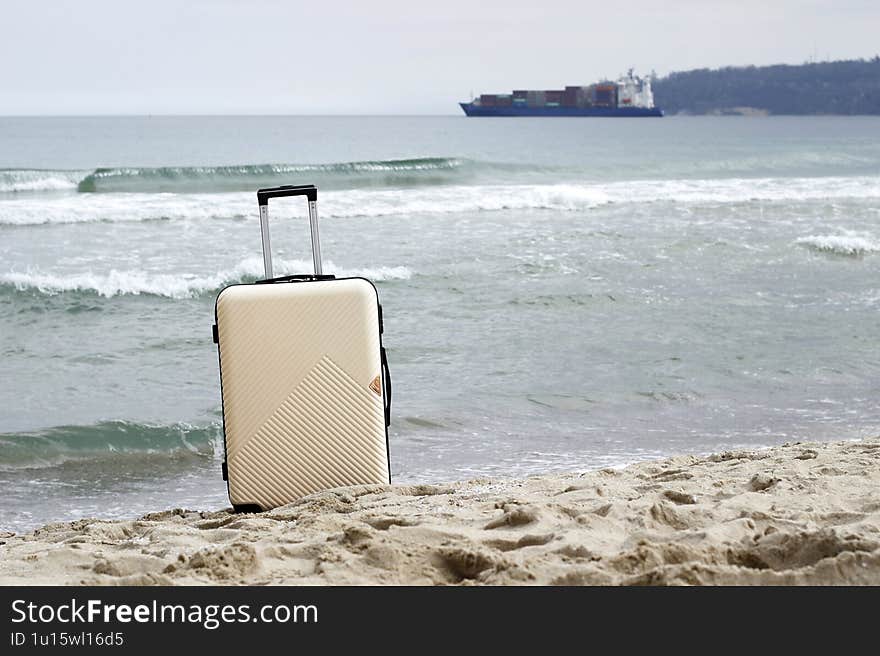A suitcase stands on a sandy beach by the sea with a cityscape in the background. Perfect for travel, vacation, and adventure concepts. Space for text.