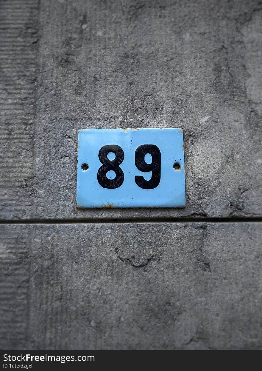 A blue sign with the number 89 (eighty nine). Against a textured stone wall