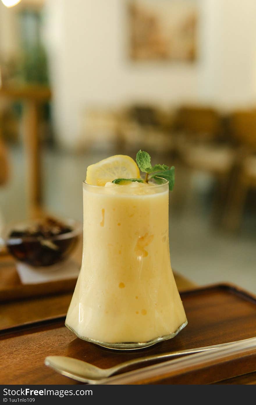 A creamy, pale yellow mango lassi fills a uniquely shaped glass, garnished with a lemon slice and mint