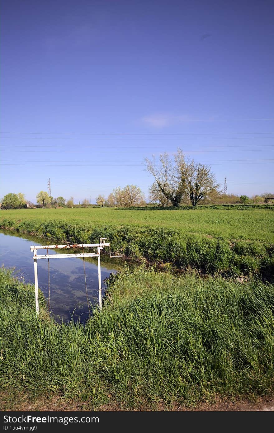 Stream of water next to a grass field with trees on the horizon on a sunny day in the italian countryside. Stream of water next to a grass field with trees on the horizon on a sunny day in the italian countryside