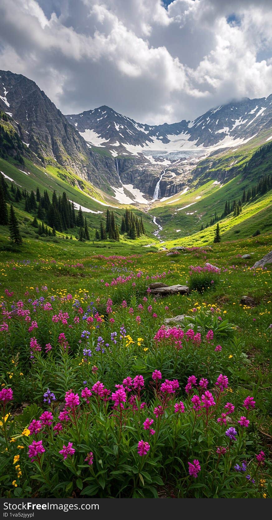 Snow-capped mountain peaks frame a lush green valley with a cascading waterfall at the center. In the foreground, a vibrant meadow blooms with pink, purple, and yellow wildflowers, possibly including species like Indian paintbrush (Castilleja) and alpine daisies. Tall evergreen trees, likely spruce or fir, line the valley, adding contrast to the vivid colors. Above, a cloudy sky casts soft shadows over the landscape, creating a dynamic scene of natural beauty. Snow-capped mountain peaks frame a lush green valley with a cascading waterfall at the center. In the foreground, a vibrant meadow blooms with pink, purple, and yellow wildflowers, possibly including species like Indian paintbrush (Castilleja) and alpine daisies. Tall evergreen trees, likely spruce or fir, line the valley, adding contrast to the vivid colors. Above, a cloudy sky casts soft shadows over the landscape, creating a dynamic scene of natural beauty.