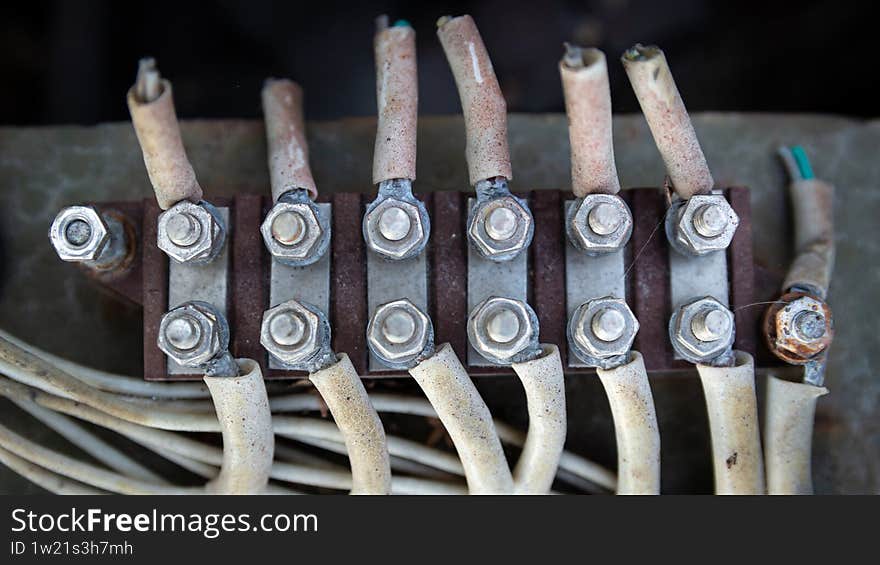 Close-up of thick, worn electrical cables with yellowed insulation, securely bolted to a terminal block