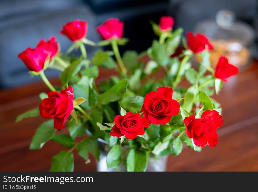 Beautiful bouquet of vibrant red roses in a glass vase placed on a wooden table. Romantic floral arrangement with lush green leaves, perfect for Valentine's Day, celebrations, or home decor themes. Beautiful bouquet of vibrant red roses in a glass vase placed on a wooden table. Romantic floral arrangement with lush green leaves, perfect for Valentine's Day, celebrations, or home decor themes.