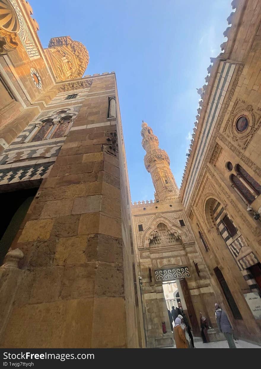 A striking upward view of a historic mosque in Cairo, bathed in golden sunlight. The intricate stone carvings, towering minaret, and grand archways reflect the elegance and depth of Islamic architecture in Egypt.