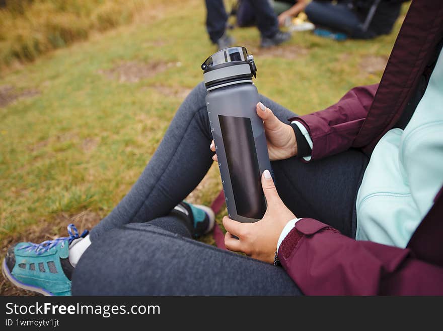 Person sitting outdoors holding a water bottle, wearing casual hiking clothing. Person sitting outdoors holding a water bottle, wearing casual hiking clothing