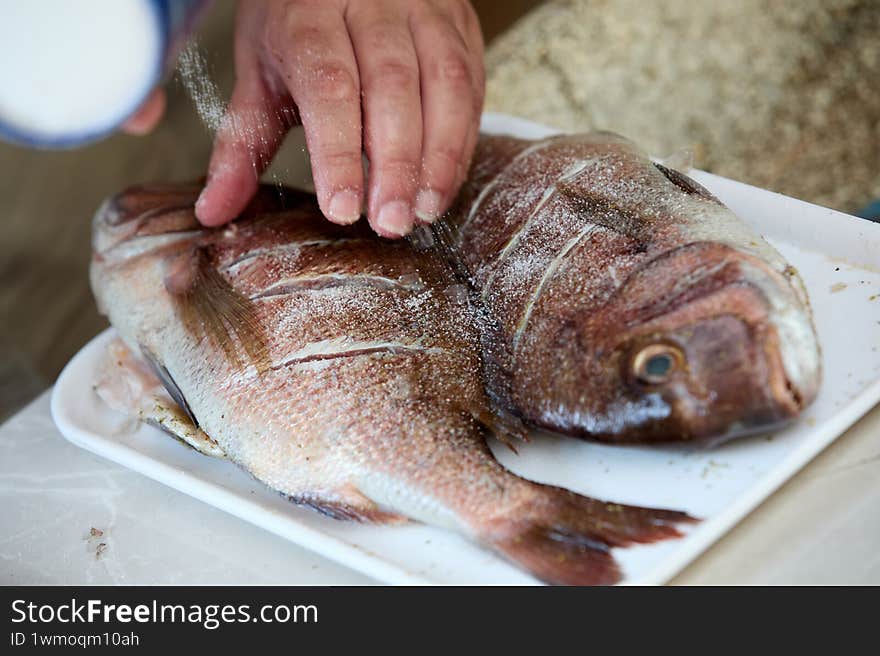 Close-up of fresh fish being seasoned by human hands, showcasing the texture of the fish and spices during preparation, highlighti