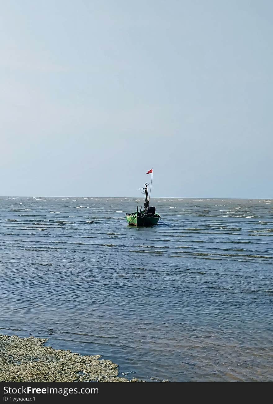 A serene view of a lone fishing boat navigating the calm waters, with gentle waves reflecting the clear sky. The Indonesian flag flutters proudly, symbolizing local maritime culture