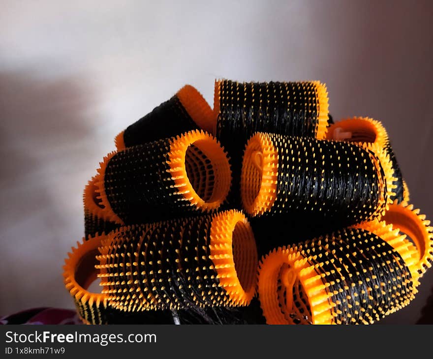 Close up of yellow plastic hair rollers or curlers and pins in African, Ghanaian woman permed hair after washing, ready for drying. Hairdressing and styling process. Rollers stuck in hair