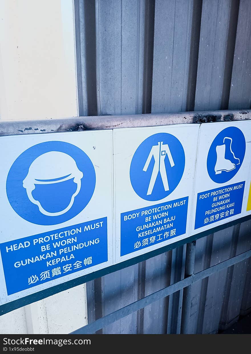 Signage illustrating the obligatory use of protective gear in a workplace, including head, body, and foot protection, highlighted with icons and multilingual text for safety and compliance.