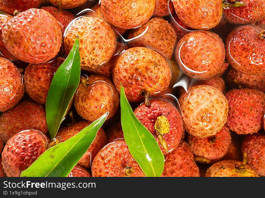 Red lychees shimmer in water, scattered with fresh green leaves.