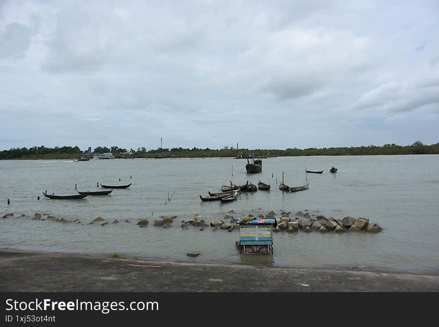 A wide view of a peaceful river scene with several traditional wooden fishing boats moored along a concrete embankment. The calm w