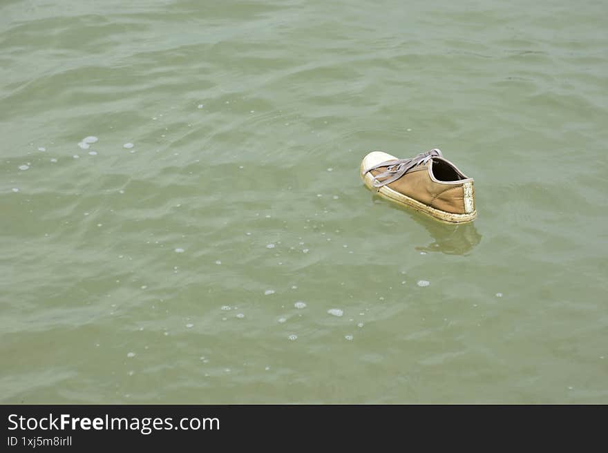 Close-up view of a lone brown sneaker with white laces drifting on the murky green surface of a pond. Surrounded by bubbles and subtle ripples, the scene evokes quiet mystery and human presence in nature. Captured near the Bakkhali River in Cox�s Bazar, Bangladesh, it reflects themes of displacement, solitude, and environmental texture in a tropical wetland.