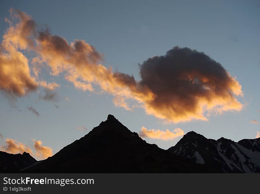 A night view of snowy mountains with clouds at sunset. The clouds and sky turn a magnificent golden color as the sun sets. An excellent choice for mountain tourism