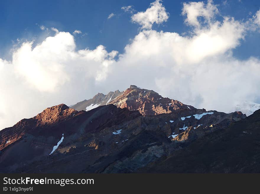 A night view of snowy mountains with clouds at sunset. The clouds and sky turn a magnificent golden color as the sun sets. An excellent choice for mountain tourism