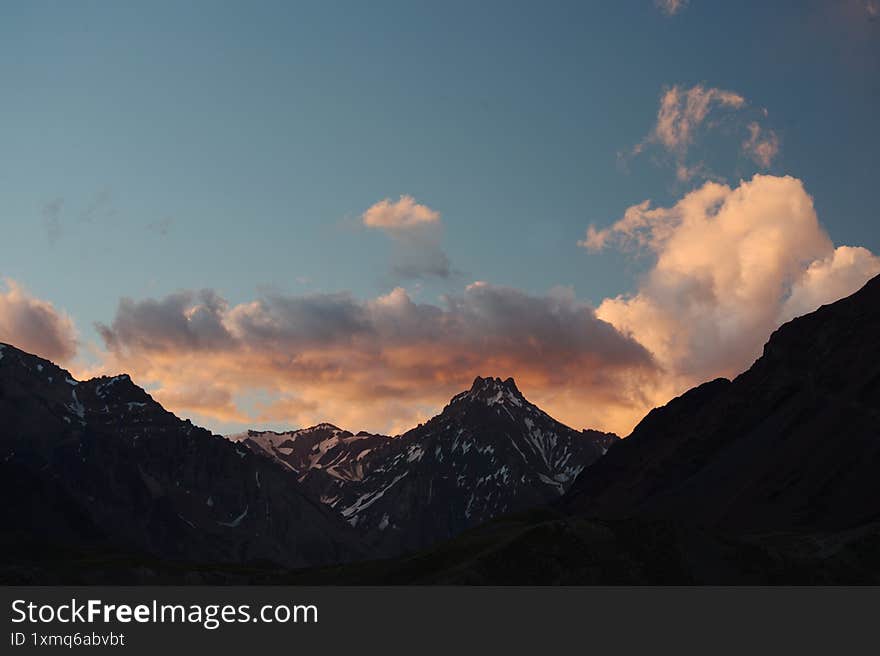 A night view of snowy mountains with clouds at sunset. The clouds and sky turn a magnificent golden color as the sun sets. An excellent choice for mountain tourism