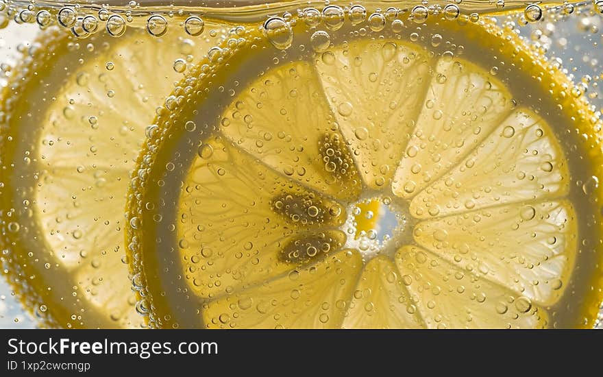 Close-up of lemon slices submerged in sparkling water with bubbles clinging to the surface.