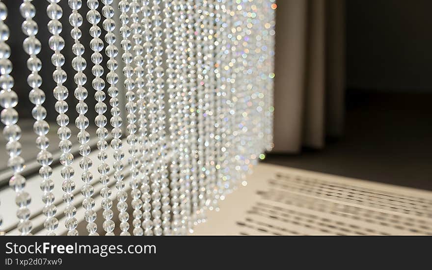Crystal bead curtain illuminated by sunlight, casting intricate shadows on the floor in a serene interior setting.