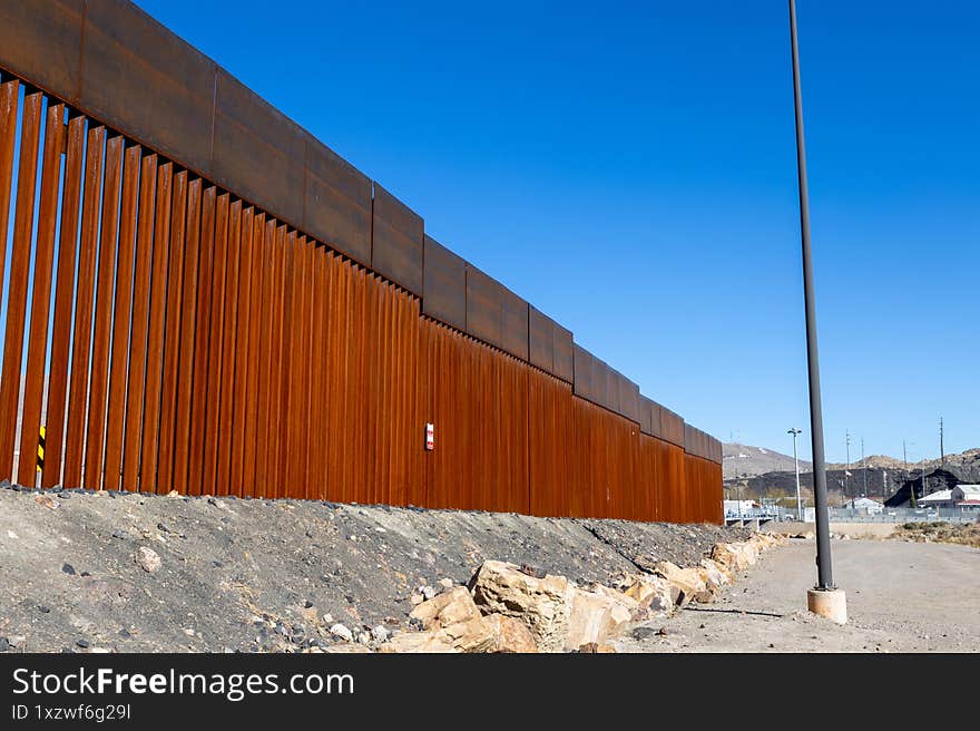 A towering wall of metal and concrete, symbol of border controversy, bisects Ciudad Juarez under an azure sky