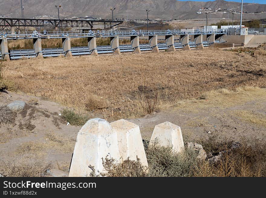 A parched riverbed in Ciudad Juarez leading to a steel gateway, signifying the challenging journey of migrants at the US-Mexico border