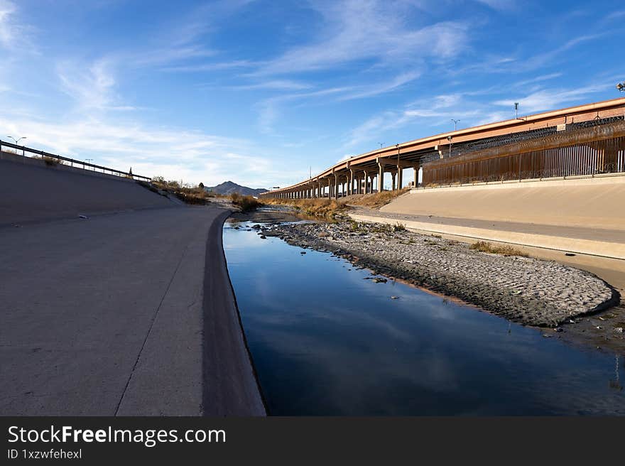 The Rio Grande, a migration route, meanders by Ciudad Juarez s border fence and under a highway, with distant mountains under a s