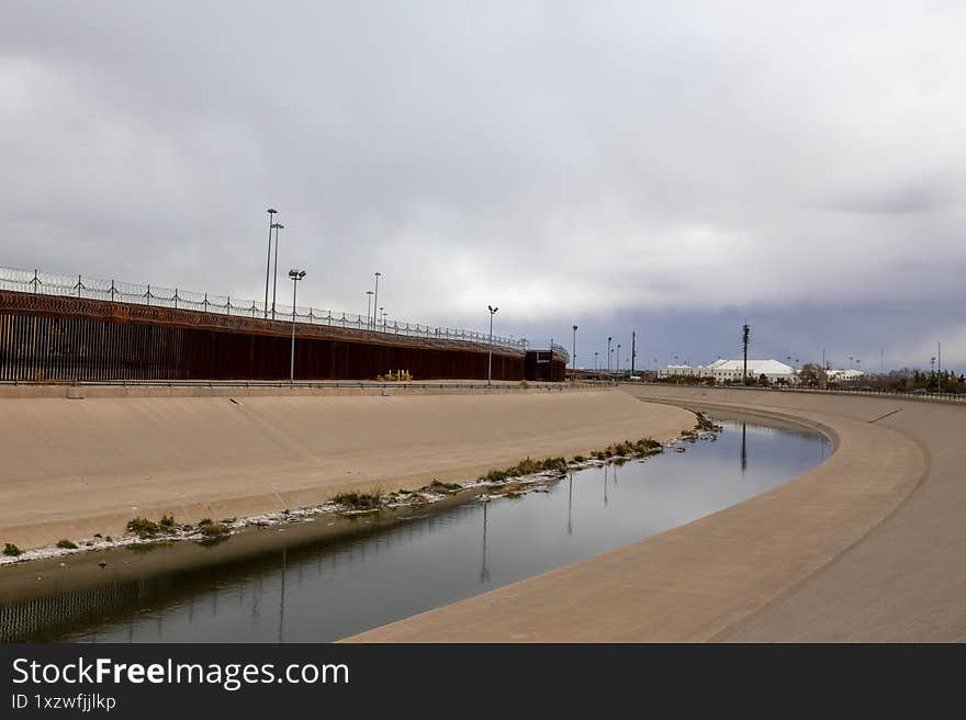 Migrants in Ciudad Juarez gaze upon the Rio Grande, its path confined by concrete, and a towering, barbed wire-laden border fence