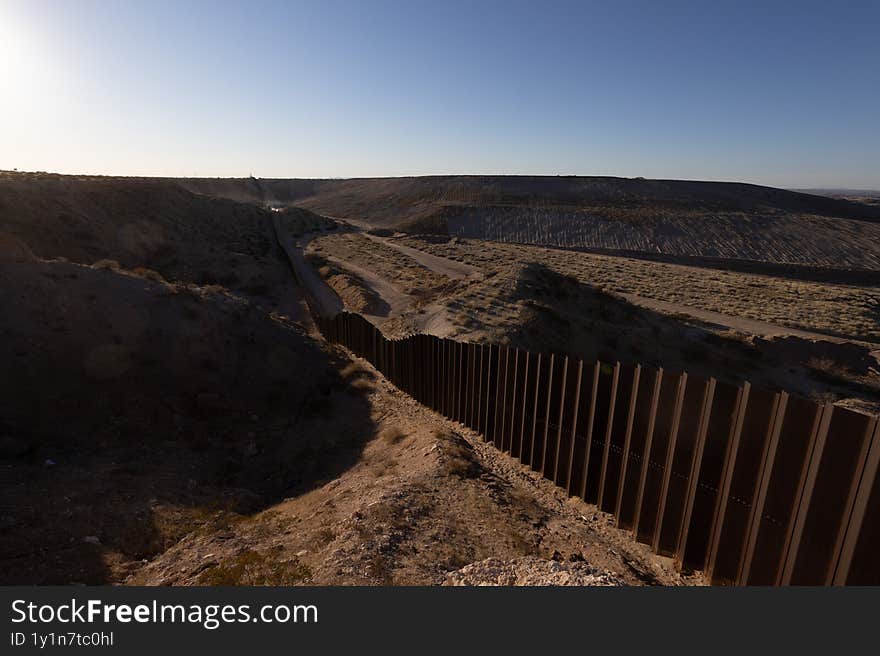 A stretch of the US-Mexico border wall, made of towering metal slats, stands amidst the arid terrain near Ciudad Juarez under azure skies