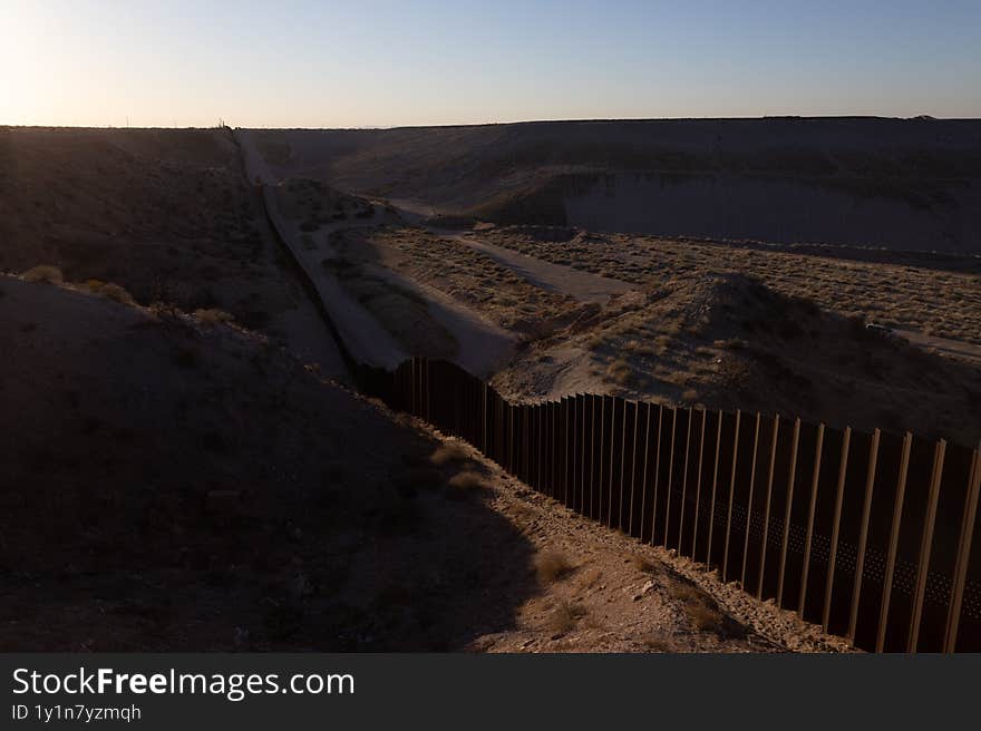 The border barrier in Ciudad Juarez divides the arid terrain at twilight, impacting migration