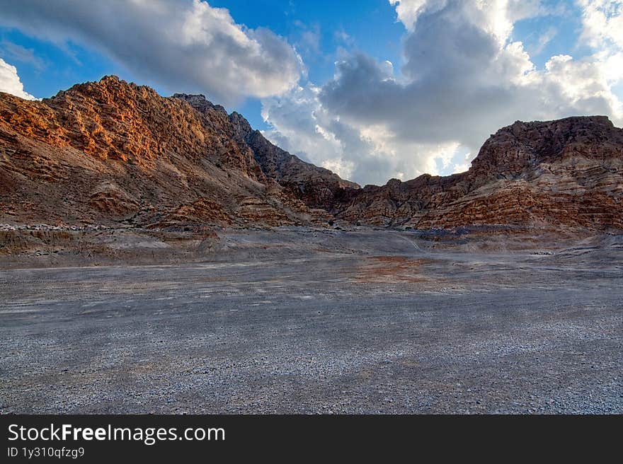 Empty desert road winding through dramatic UAE mountain ranges, creating strong leading lines under clear blue skies. Limestone formations and arid valleys evoke raw natural beauty. Perfect for adventure travel campaigns, automotive ads, or metaphor visuals about life journeys