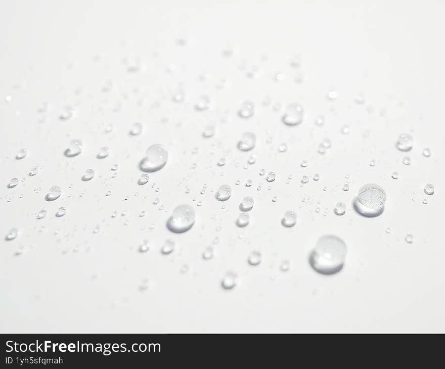 Clear water droplets scattered on a bright white surface