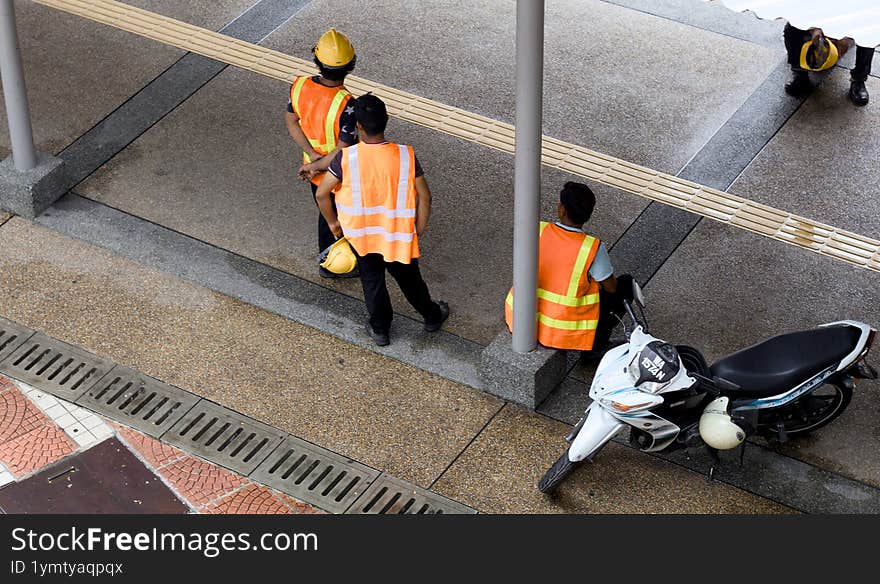 three construction workers taking a break on an urban walkway.