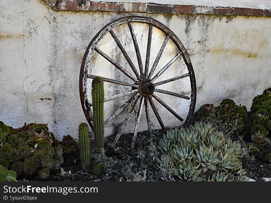 old western wagon wheel leaning next to a brick wall with cactus plants