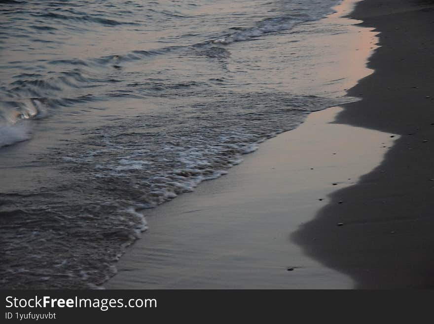 The calming rhythm of the ocean at dusk, with faint figures enjoying the water.