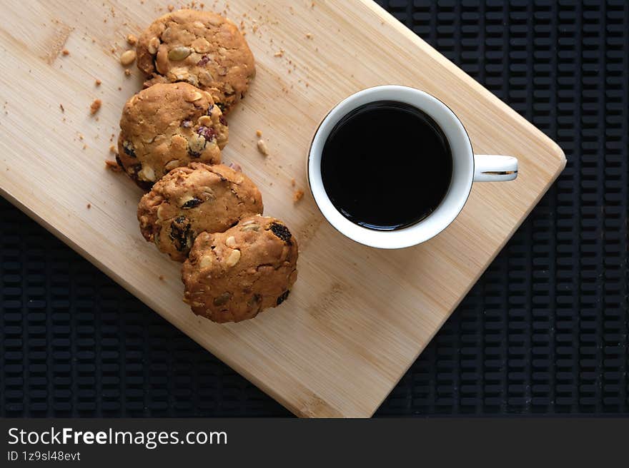 Homemade cookies with nuts and dried fruits served on a wooden board alongside a cup of black coffee. Perfect for breakfast, snack