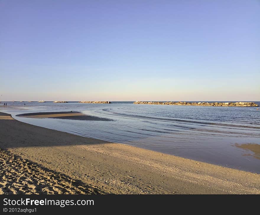 Beach at sunset with a breakwater in the distance on a clear day