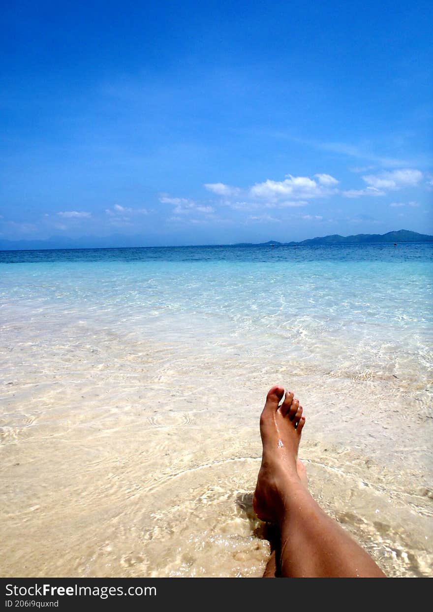 the feet of a person lying on the beach facing the open sea