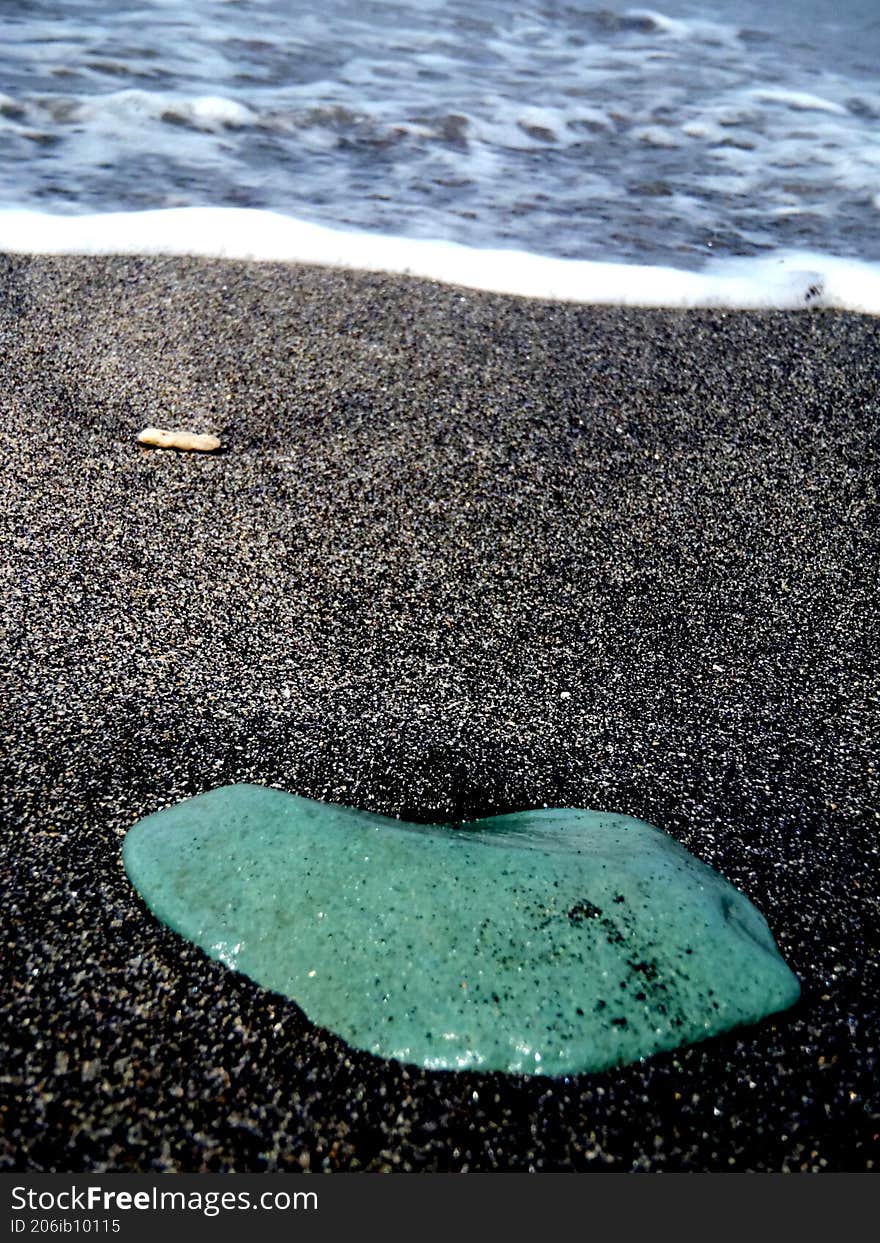 a green small stone on a black sand at the beach