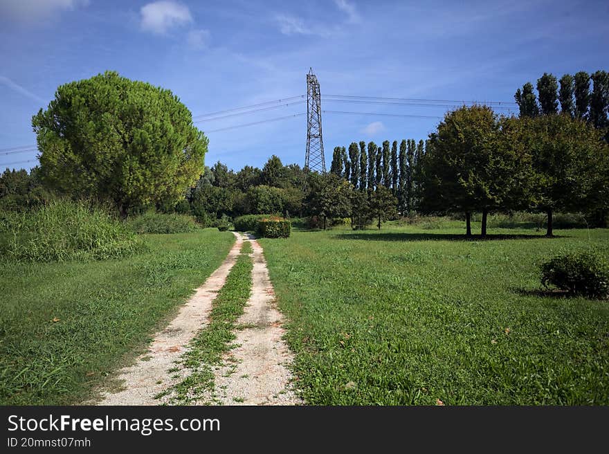 Rock trail in a park with trees bordering it and an electricity mast in the background on a sunny day in the italian countryside. Rock trail in a park with trees bordering it and an electricity mast in the background on a sunny day in the italian countryside