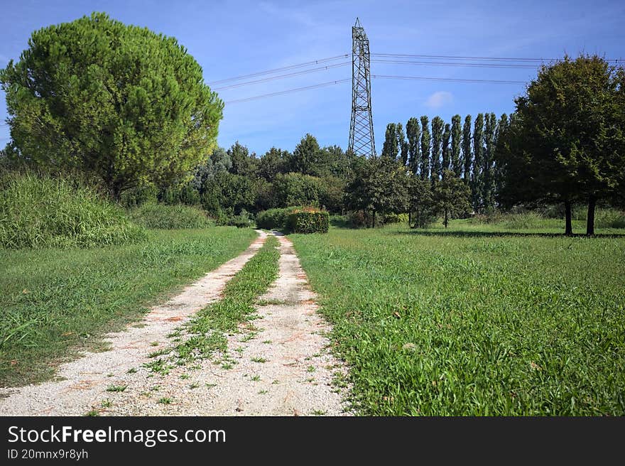 Rock trail in a park with trees bordering it and an electricity mast in the background on a sunny day in the italian countryside. Rock trail in a park with trees bordering it and an electricity mast in the background on a sunny day in the italian countryside