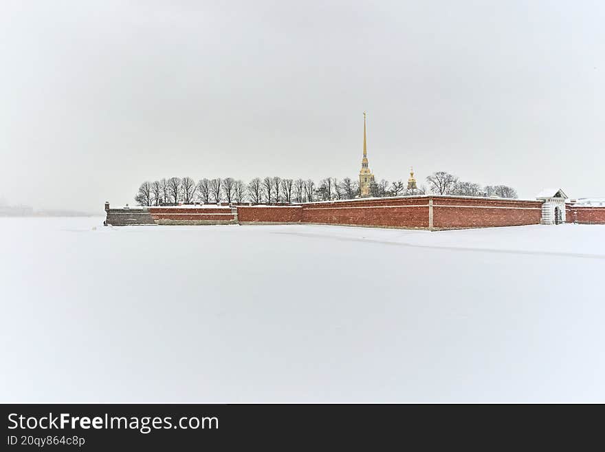 Wide shot of the Peter and Paul Fortress in snowy weather. Stark contrast between the red brick wall and the snow-covered Neva field. A unique historical and tourist attraction. Ideal for history, winter, and architecture themes